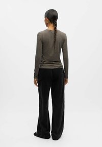 Maglietta a maniche lunghe di colore verde oliva abbinata a pantaloni ampi neri con texture. Vista posteriore che mostra una vestibilità snella e una silhouette rilassata.