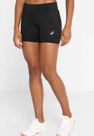 Athlete wearing black fitted shorts with logo on left thigh and white running shoes with peach accents on a white background.