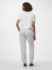 T-shirt bianco croppato e pantaloni tuta grigi con polsini elastici, abbinati a sneakers nere con accenti a forma di cuore. Tessuto morbido, vestibilità comoda.