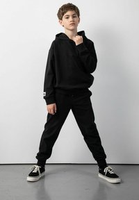 Czarna bluza z kapturem i pasujące spodnie dresowe z teksturowanej tkaniny, charakteryzujące się luźnym krojem i elastycznymi mankietami, połączone z czarnymi trampkami.