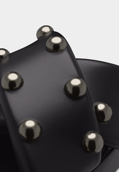 Gros plan sur une sangle en cuir noir ornée de rivets argentés polis ronds disposés en rangées.