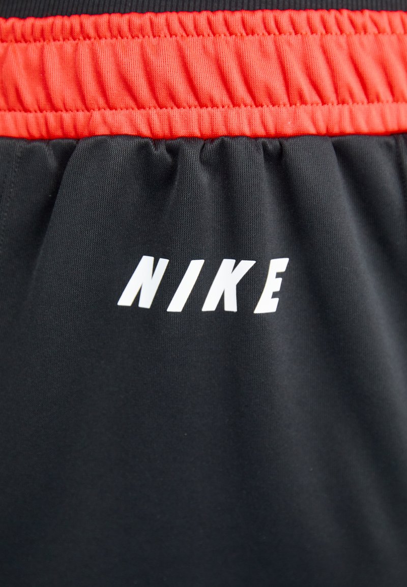 Shorts negros con una cinturilla elástica roja presentan un audaz logo blanco de "NIKE" en la parte frontal. El material parece suave con un ligero brillo.