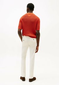 Rød strikket polo skjorte med korte ærmer og V-hals design, parret med hvide slim-fit bukser og brune loafers.