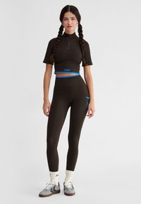 Brun ribbad crop top med korta ärmar och dragkedjekrage, kombinerad med matchande högmidjade leggings med blå detaljer.