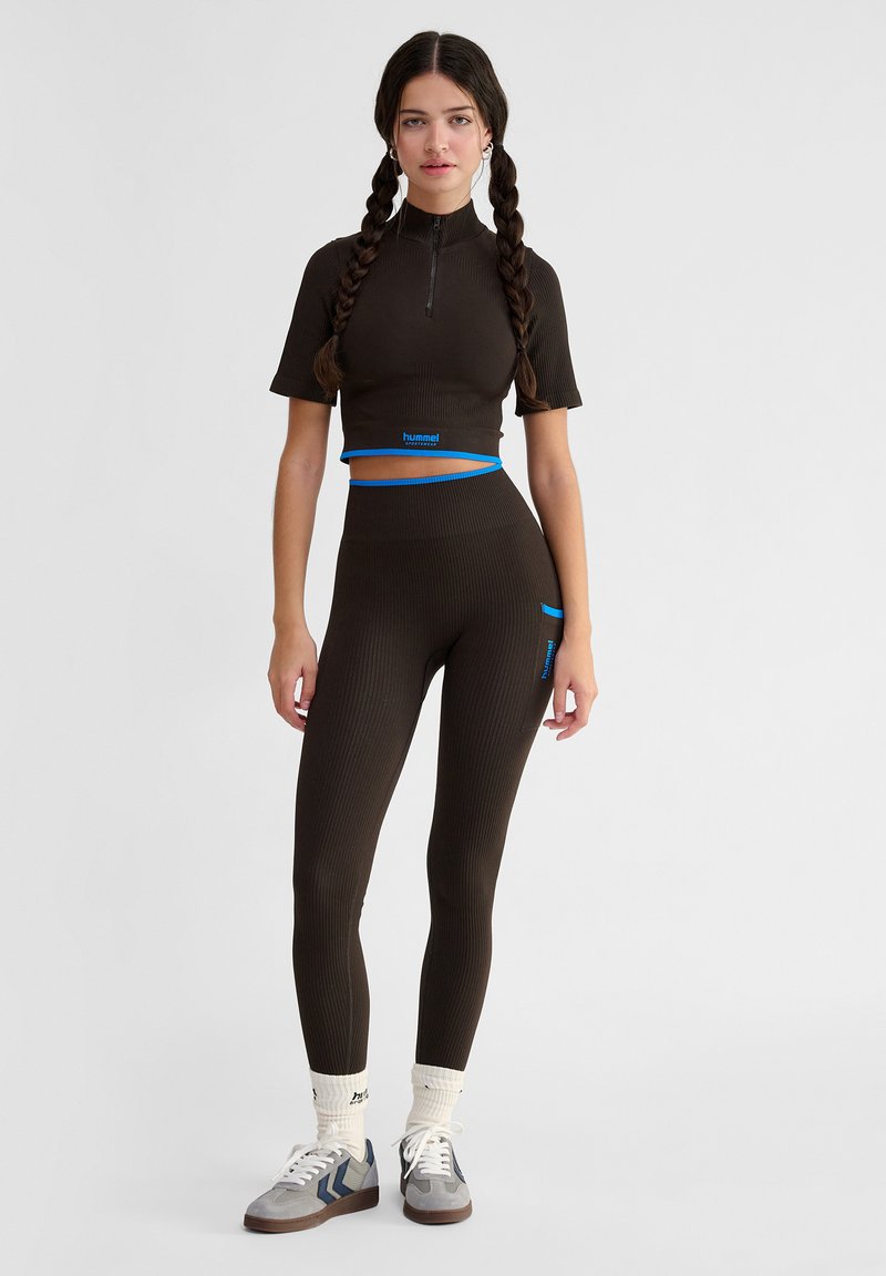 Brun ribbad crop top med korta ärmar och dragkedjekrage, kombinerad med matchande högmidjade leggings med blå detaljer.