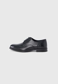Chaussure Oxford en cuir noir pour homme, avec laçage fermé et talon bas, présentée en profil droit sur un fond gris clair uni.