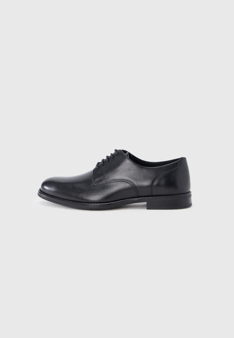 Chaussure Oxford en cuir noir pour homme, avec laçage fermé et talon bas, présentée en profil droit sur un fond gris clair uni.