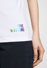 White cotton t-shirt featuring multicolored embossed text "LOVE MOSCHINO" near the hem. Simple design with a comfortable fit.