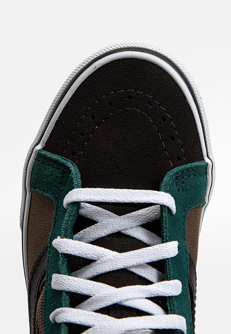 Baskets noires et marron avec des accents en daim vert. Dotées de lacets blancs et d'une semelle en caoutchouc, présentant un renfort à l'avant et des détails piqués.