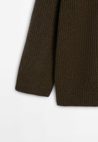 Manche côtelée tricotée marron foncé et ourlet d'un pull en laine sur fond blanc.