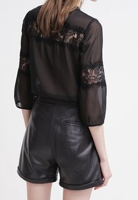 Czarna przezroczysta bluzka z koronkowymi zdobieniami na ramionach i rękawach, zestawiona z czarnymi, skórzanymi szortami z wysokim stanem. Gładka faktura, swobodny design.
