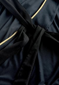 Must mustriga kangas, millel on sile tekstuur, kuldse äärise ja keskel seotud detailidega. Materjal näeb välja pehme ja langeb elegantselt.