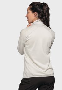 Hellgraue, langärmelige Sportjacke mit hohem Kragen, strukturiertem Stoff und einer seitlichen Reißverschlusstasche.