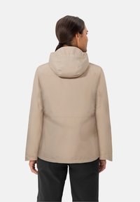 Giacca impermeabile beige con cappuccio, caratterizzata da un design minimalista e una texture liscia, vista da dietro. Sotto sono indossati pantaloni neri.