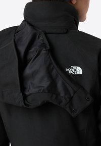 Giacca nera con colletto alto, dotata di tasca interna con zip e logo bianco sul retro. Tessuto esterno liscio con finitura opaca.