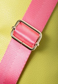 Materiale verde texturizzato con una larga cintura rosa e una fibbia dorata lucida, che mette in mostra trame lisce e intrecciate.