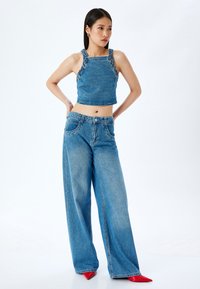 Top corto de denim con tirantes adornados, combinado con jeans de pierna ancha y cintura alta en un lavado azul claro y zapatos de tacón rojo de punta. 