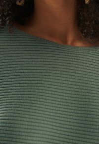 Zielony prążkowany top z fakturowaną powierzchnią i szerokim dekoltem, prezentujący poziome linie i miękką tkaninę.