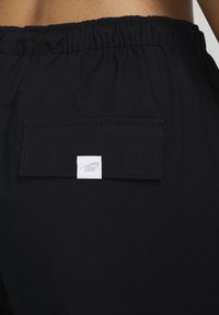 Černé sportovní šortky mají strukturovanou tkaninu, elastický pás a zadní kapsu se štítkem bílého loga Nike.
