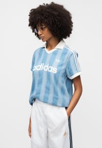 Polo Adidas rayé bleu clair avec un col blanc ; il présente un grand logo blanc et trois rayures blanches sur les manches.