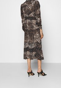 Långärmad klänning i leopardmönster i mörka toner med åtsittande midja och längd till mitten av vaden, som matchas med svarta öppna klackar.