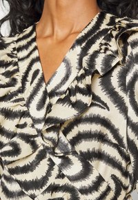 Black and cream patterned top featuring ruffles along the neckline and a fluid, textured fabric with a swirling design.