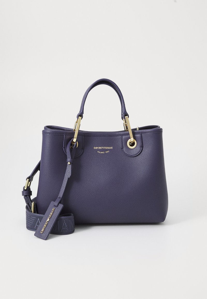 Purple leather handbag with gold hardware, featuring two handles and a detachable strap. Embossed logo on the front adds branding detail.