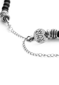 Black beaded necklace featuring metal accents, large textured rings, and a circular charm engraved with "WAY". Silver chain for closure.
