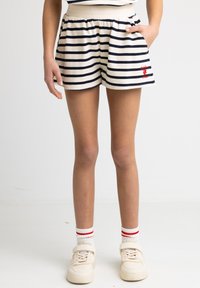 Spodenki w paski z elastycznym pasem w odcieniu beżowym i granatowym, z boczną kieszenią i haftowanym czerwonym detalem, w zestawie z białymi skarpetkami i trampkami.