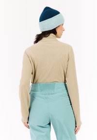 Beige top met lange mouwen en een hoge kraag, gecombineerd met aqua broek met een geribde taille. Blauw en lichtblauw gebreide beanie op het hoofd.