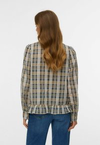 Blusa a quadretti beige, blu e nera, con orlo arricciato e maniche a sbuffo. Realizzata in tessuto leggero adatta per un abbigliamento casual.