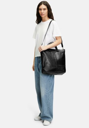 Sac fourre-tout en cuir noir avec un design structuré, des poignées supérieures et une bandoulière ajustable. Texture lisse et détail de logo embossé.