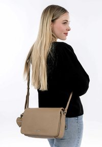 Sac à bandoulière en cuir tan avec une finition texturée, fermeture à rabat, sangle réglable et une étiquette en forme de cœur.
