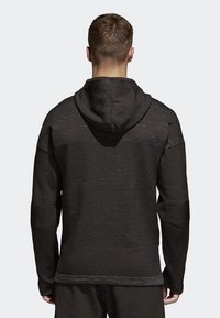 Svart hoodie med texturerad stickad tyg, utrustad med en dragsko på huvan och mjuka mudd. Designen är enkel med minimala detaljer.