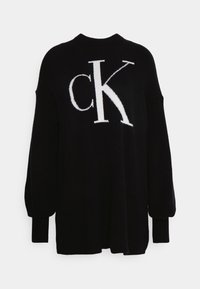 Pull en maille noire avec un grand logo blanc « CK » sur le devant, des poignets côtelés, et une coupe décontractée avec des épaules tombantes.
