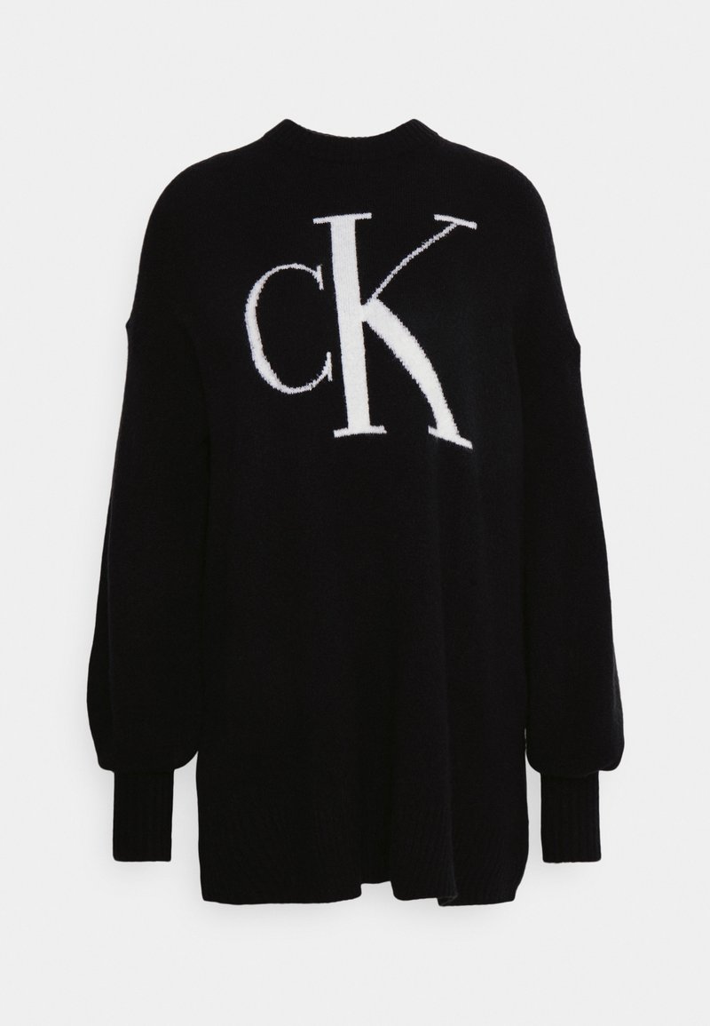 Pull en maille noire avec un grand logo blanc « CK » sur le devant, des poignets côtelés, et une coupe décontractée avec des épaules tombantes.