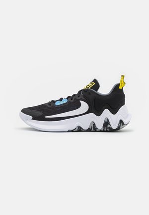 Sort og hvid sportssko med stort hvidt swoosh-logo, bølget såldesign, gul træksløjfe og lyseblå snøredetalje.