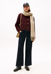 Bordeaux cropped jack met gouden knopen, gestreepte top, wijde donkerdenim jeans, beige sjaal en zwarte enkelboots. Kleine bruine schoudertas.