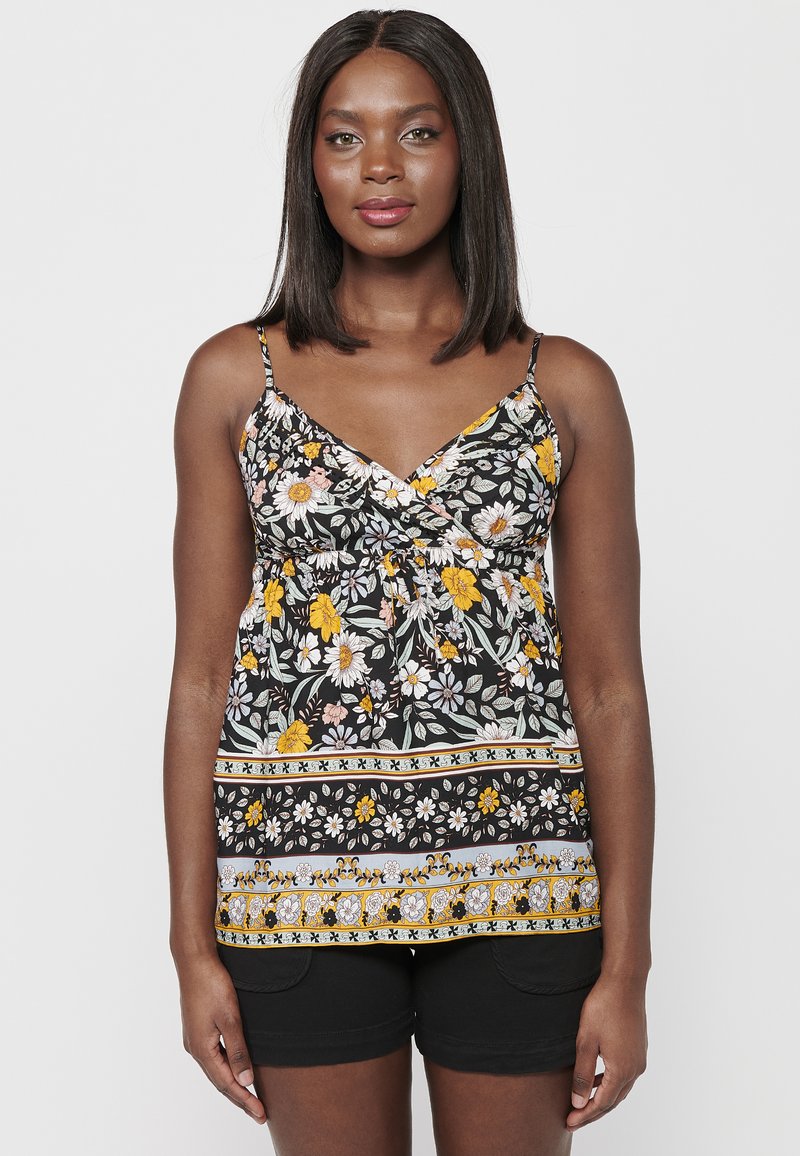 Musthave lille mustriga tank top musta värvi, millel on kollased, roosad ja valged lilled. Omab õhukesi rihmasid, mähisdisaini ja mustriga äärist. Koos mustade lühikeste pükstega.