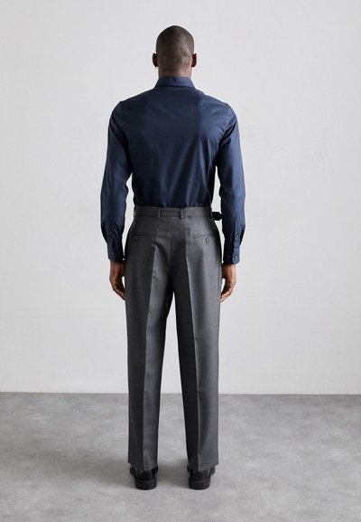Chemise marine à manches longues avec poignets à boutons, associée à un pantalon gris ajusté, présentant un devant plat et des jambes droites, portée avec des chaussures noires.