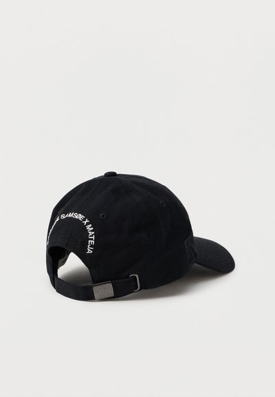 Casquette de baseball noire réglable avec boucle en métal et texte brodé blanc près de l'ouverture arrière, montrée sous un léger angle sur fond uni.