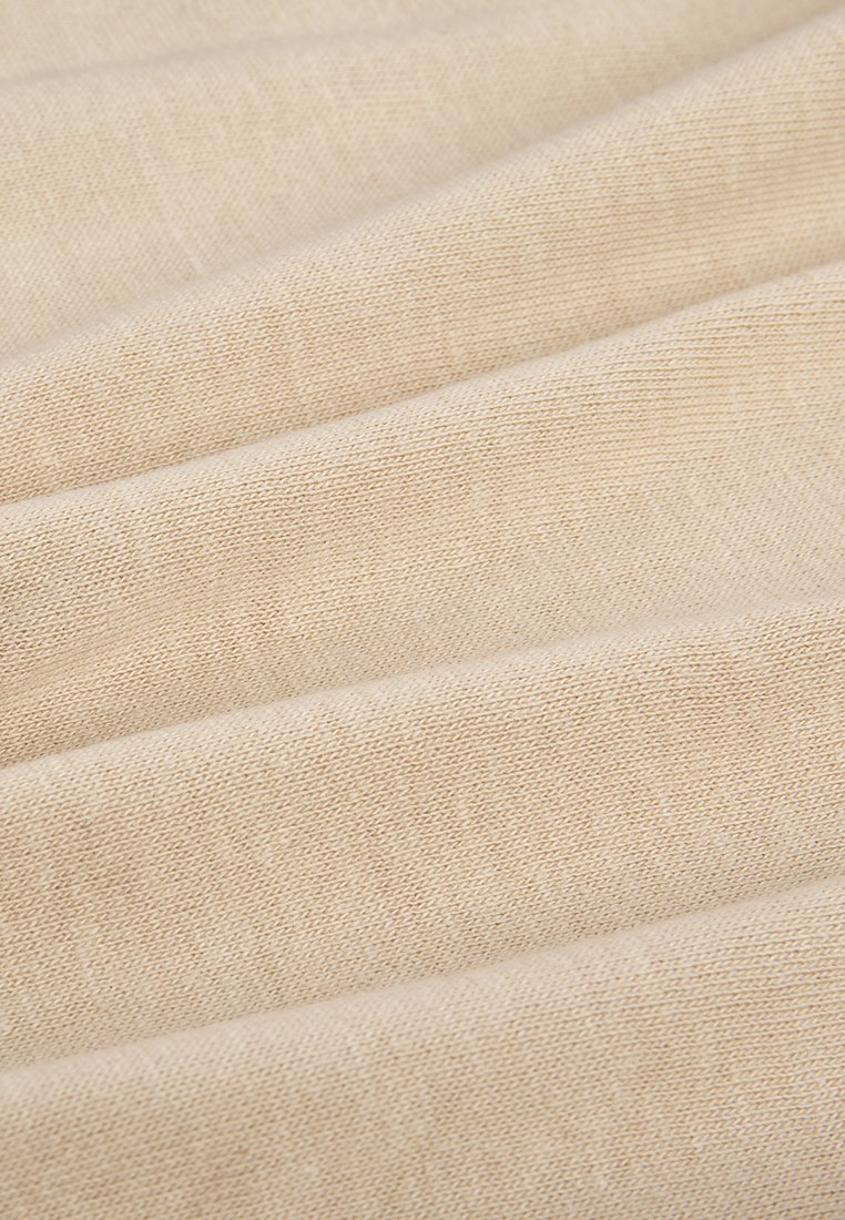 Tessuto beige con una consistenza liscia, che presenta un sottile motivo di tessitura. Le pieghe creano onde delicate, riflettendo la luce dolcemente sulla superficie.