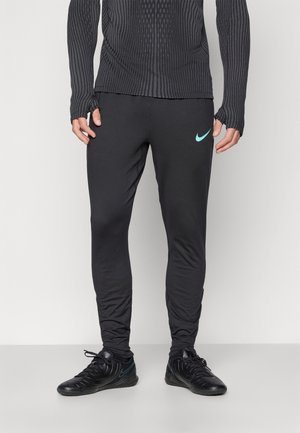 Zwarte sportbroeken met een slim fit, gemaakt van een gladde stof. Voorzien van een klein turquoise Nike-logo op de linkerdij. G gedragen met zwarte sportschoenen.