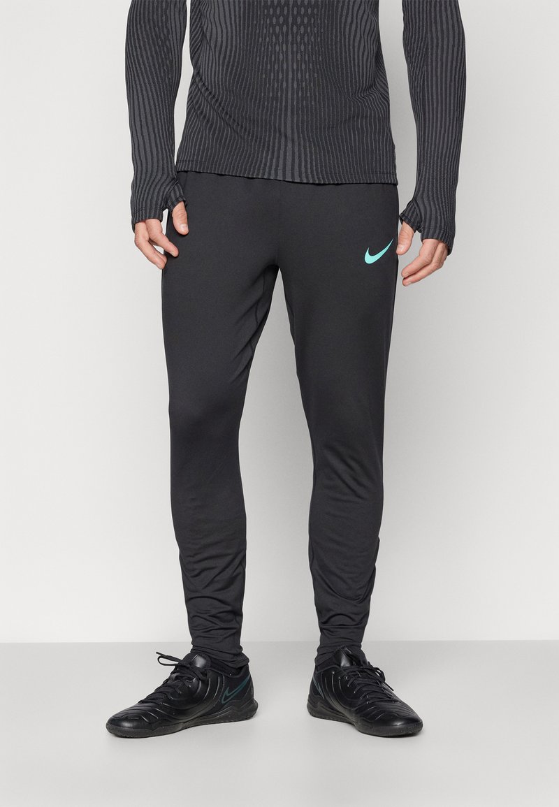 Zwarte sportbroeken met een slim fit, gemaakt van een gladde stof. Voorzien van een klein turquoise Nike-logo op de linkerdij. G gedragen met zwarte sportschoenen.