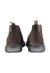 Paar donkerbruine suède enkellaarzen met zwarte dikke zolen en gestreepte stoffen uittreklussen, gezien van achteren op een witte achtergrond.