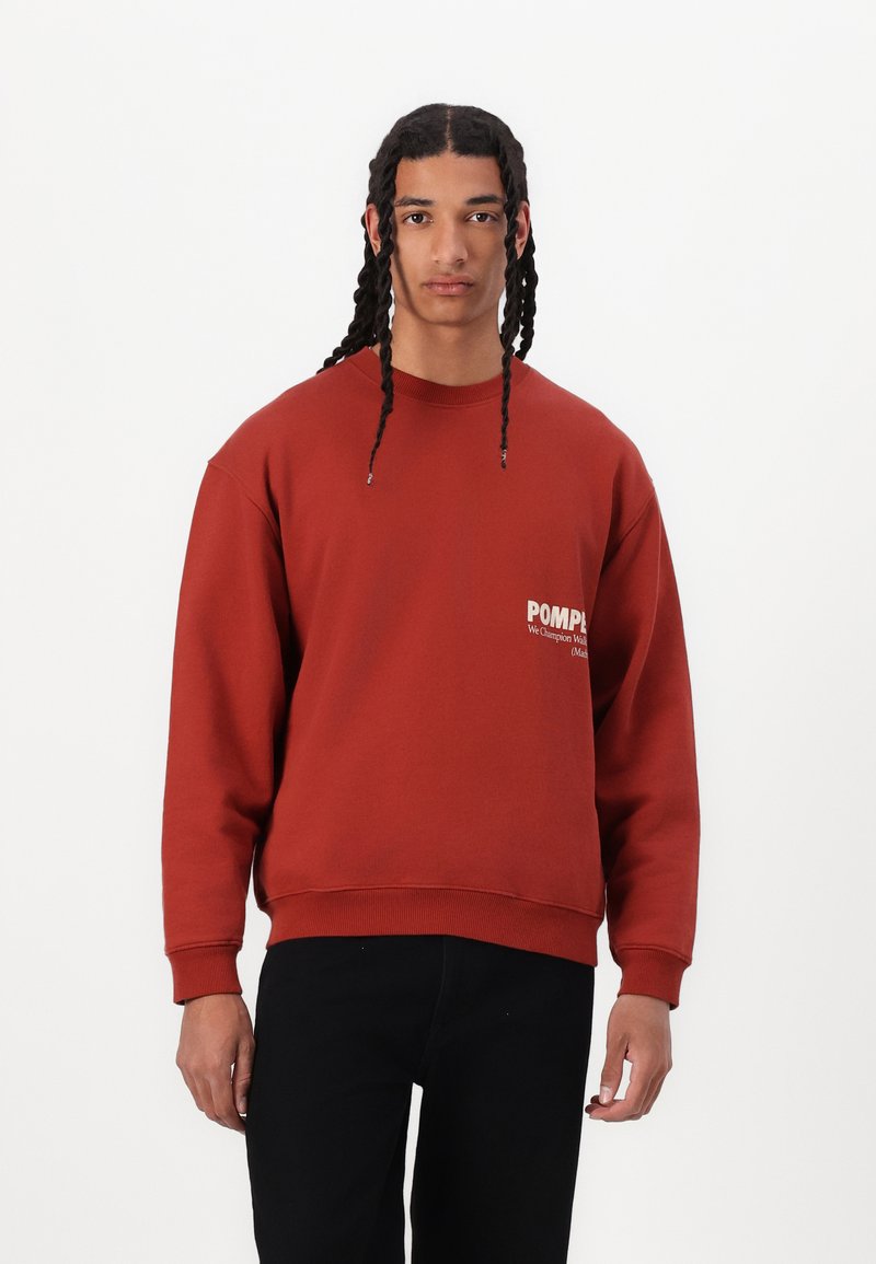 Rustfarget hettegenser med rund hals, ribbestrikkede mansjetter og brodert logo på brystet. Mykt stoff med avslappet passform.