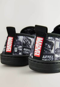 Sorte slip-on sko med et tegneserie-mønster med Marvel-figurer. Sorte gummisulder, stof-overdel og røde mærketags på hælen.