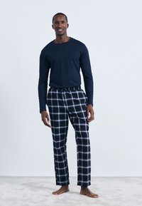 Mornarska majica dugih rukava u kombinaciji s crno-bijelim kariranim flanelskim hlačama s elastičnim strukom i vezicom, mekog tekstila.