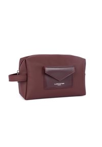 Borsa cosmetica bordeaux realizzata in materiale liscio, con tasca anteriore a pattina, chiusura con cerniera e maniglia laterale per un facile trasporto.