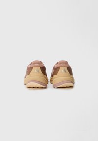 Achteraanzicht van bruin en roze sportschoenen met een gestructureerd mesh-bovenwerk, rubberen zool en een drie-strepen logo. Kenmerken zijn de gevoerde hak en contrasterende accenten.